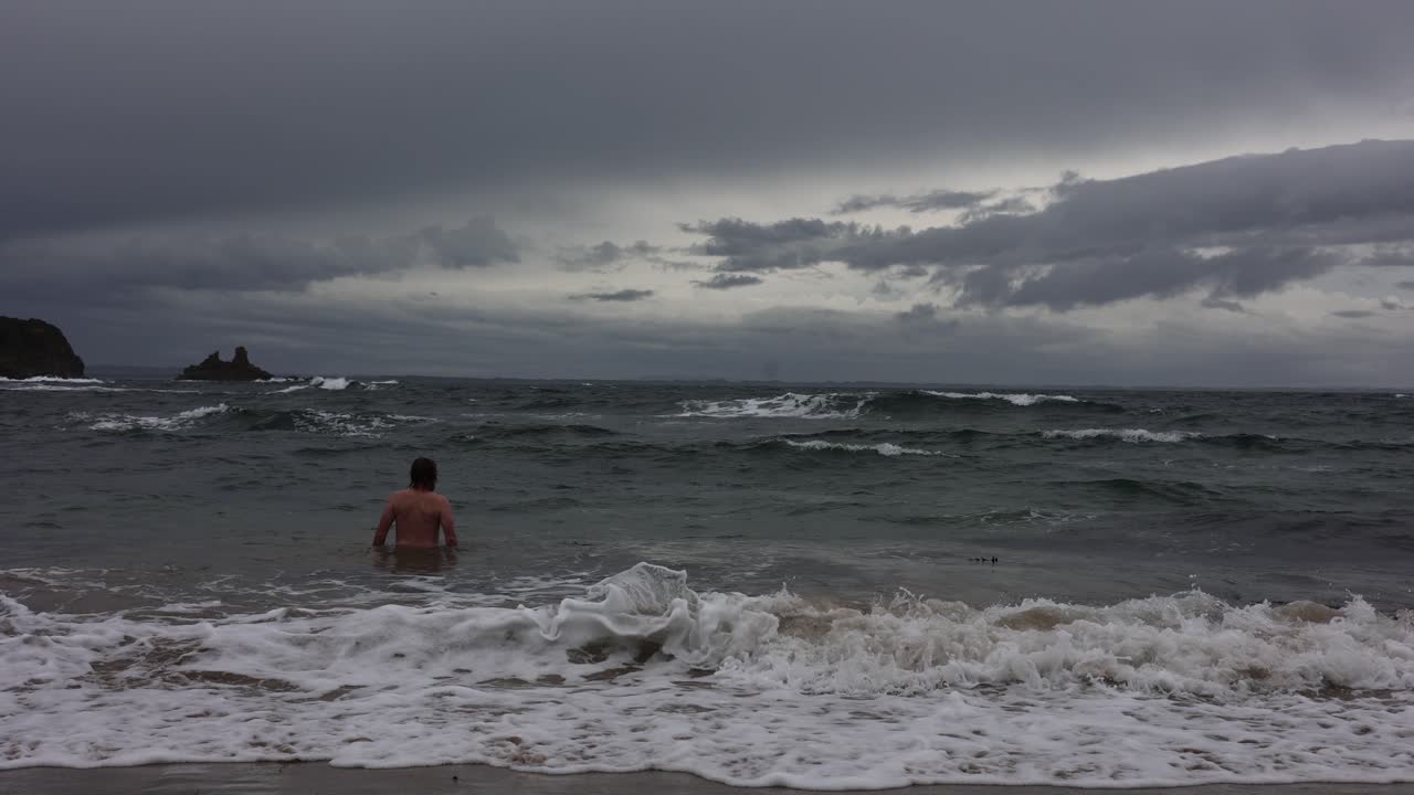 폭풍우 치는 파도 속으로 들어가 겨울에 수영하는 수염 난 남자의 슬로우 모션 샷