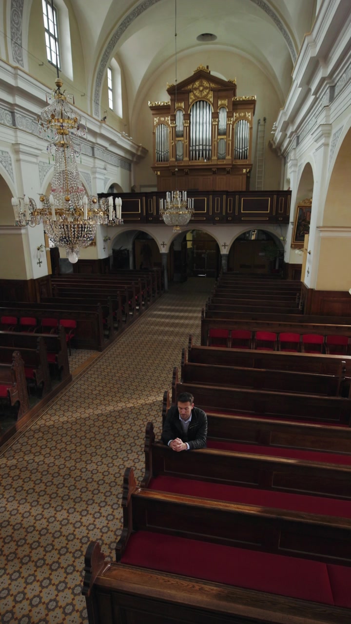Uomo sereno, un credente, che si muove in una chiesa cattolica vuota, inchinandosi verso l'altare e prendendo posto in un banco.