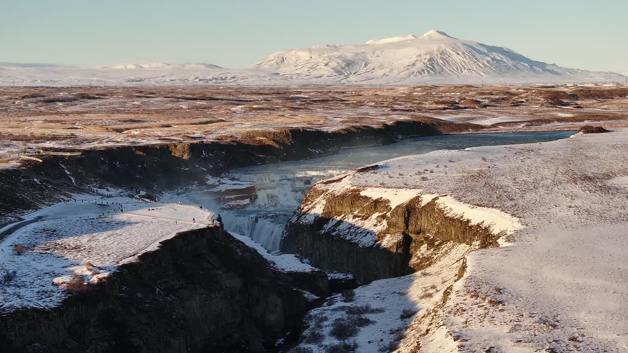 Aerial view of Gullfoss waterfall in Iceland’s South Region, where the Hvítá River plunges into a deep canyon. Snow-covered landscapes and distant mountains frame this dramatic winter scene.