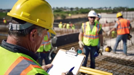 workers at a construction site review plans and document progress while others work nearby. the team collaborates under clear skies, ensuring safety and efficiency.