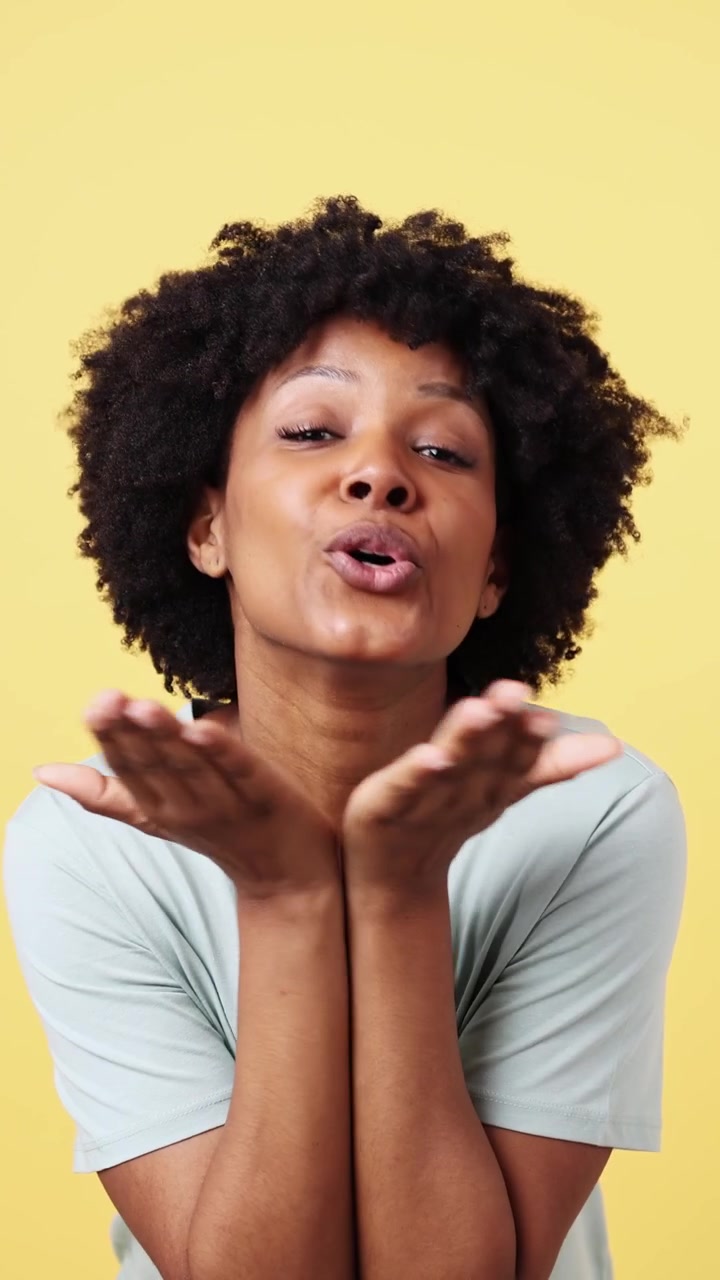 Young African American Woman Blowing a Kiss and Smiling on Yellow Background