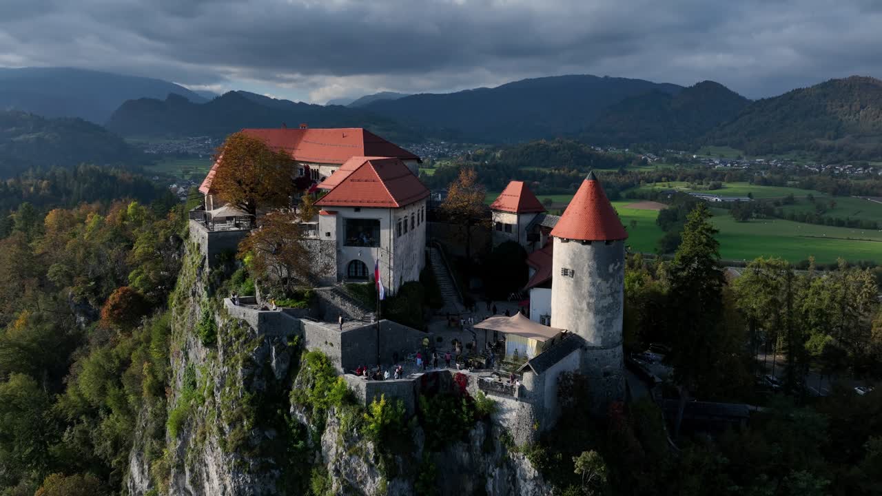 Panoramica aerea ravvicinata che circonda il Castello di Bled sopra il Lago di Bled con colline boscose e paesaggio alpino in Slovenia