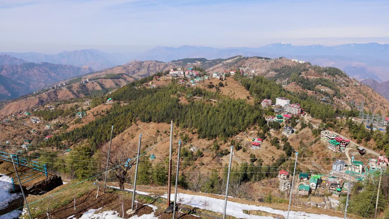 रेलिंग और लटकते गमलों वाली बालकनी से पहाड़ी शहर को देखते हुए पर्वतीय घाटी का दृश्य।