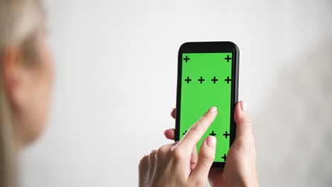 la chica tiene en las manos el iphone y desliza, desliza la pantalla de anuncios de chromakey de maqueta verde.