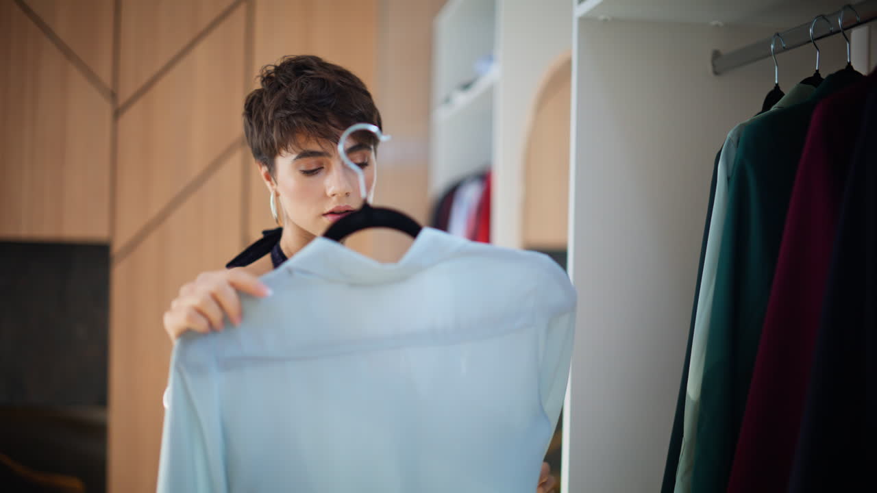 Donna bruna che sfoglia gli appendiabiti scegliendo i vestiti in una grande e luminosa cabina armadio, primo piano.