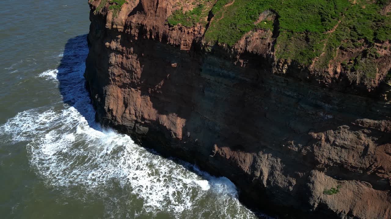 el aumento de los drones revela grandes olas oceánicas que se estrellan en acantilados rocosos en un soleado día de verano en la costa norte de yorkshire en staithes