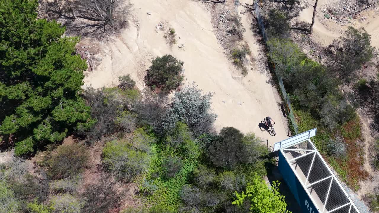 Un drone riprende un ciclista che attraversa un ponte su un sentiero sterrato a Canberra