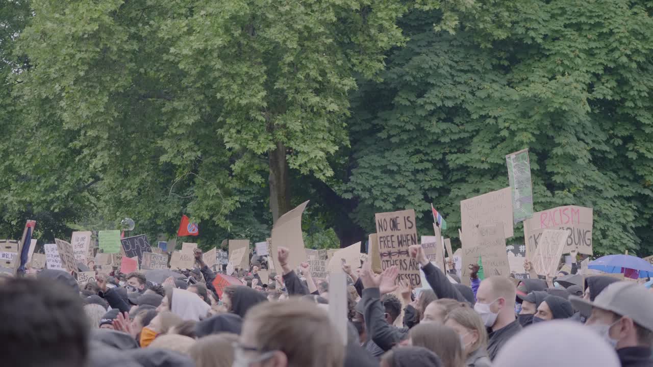 Huge racially diverse crowd of protestors raising fists and holding up signs against racism during a black lives matter protest in the rain in Stuttgart Germany.