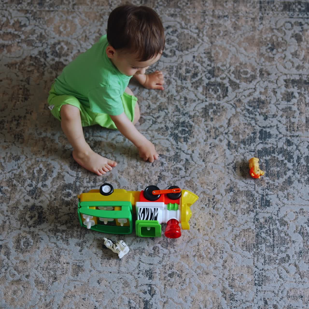 One year old toddler sitting on the carpet in the room. Dark-haired boy plays with the toy train. Top view