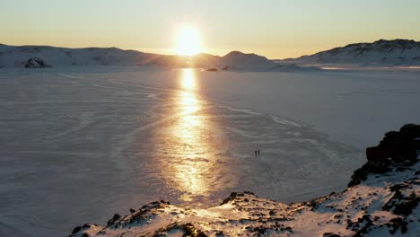 personas caminando por el lago congelado con el atardecer y los reflejos de los rayos del sol