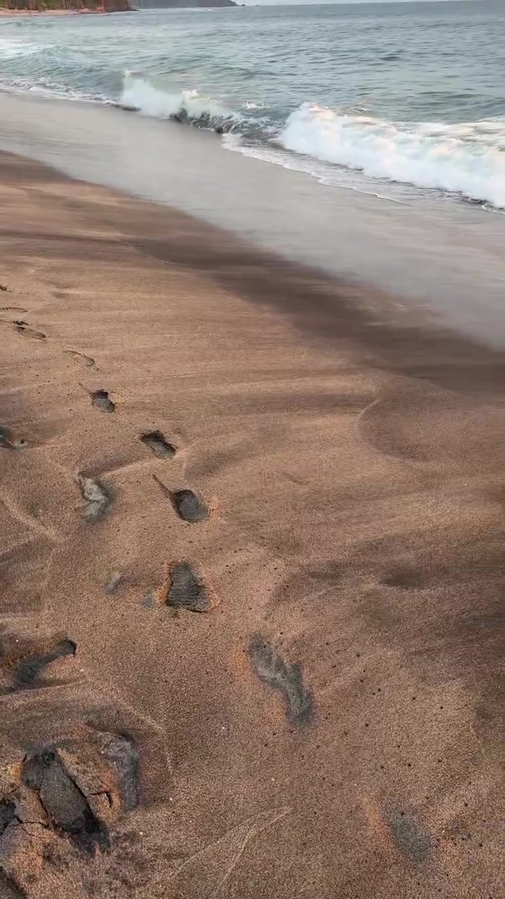 Impronte su spiaggia sabbiosa che conducono alle onde del mare in arrivo