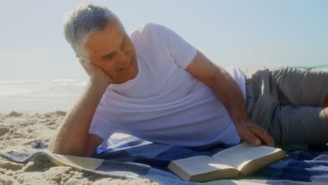 Vista-Frontal-De-Un-Hombre-Caucásico-Senior-Activo-Leyendo-Un-Libro-En-La-Playa-4k