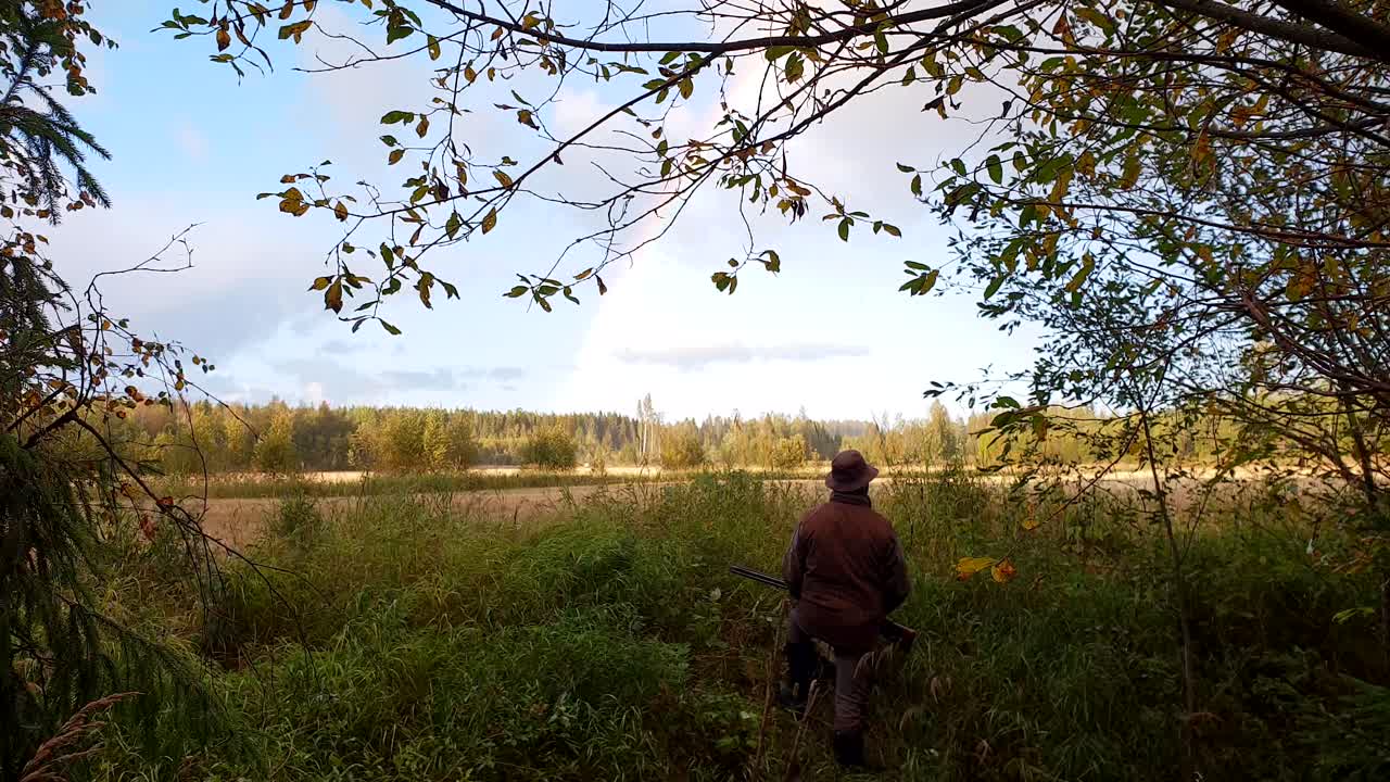 Hunter man with shotgun waits patiently while enjoying beautiful rainbow and scenery