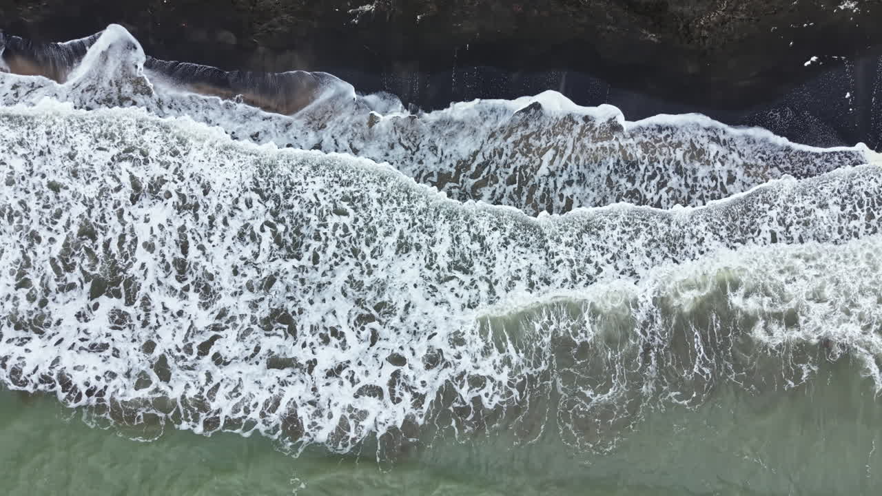Waves crash on a rocky shore under cloudy skies at a coastal area in the early evening