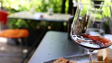 close-up of red wine swirling in a glass on a sunny outdoor table.