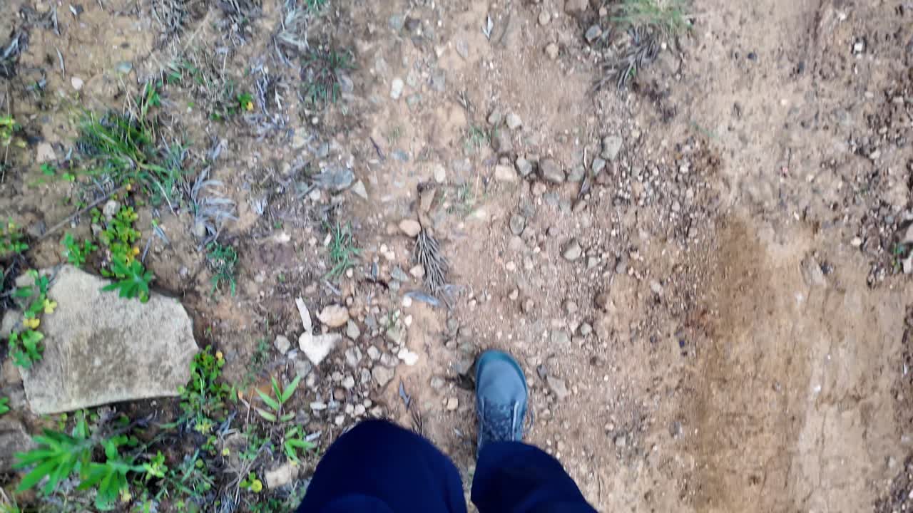 Toprak bir patika boyunca yürüyen ayakların yukarıdan görünümü, doğal bir yoldaki yolculuğun özünü yakalıyor. Sahne, vahşi doğada bir macera ve keşif hissi uyandırıyor.