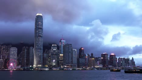 a stationary wide angle footage of a star ferry passenger transport vessel while it cruises along the victoria harbour on a cloudy day along the buildings and skyscrapers in hong kong