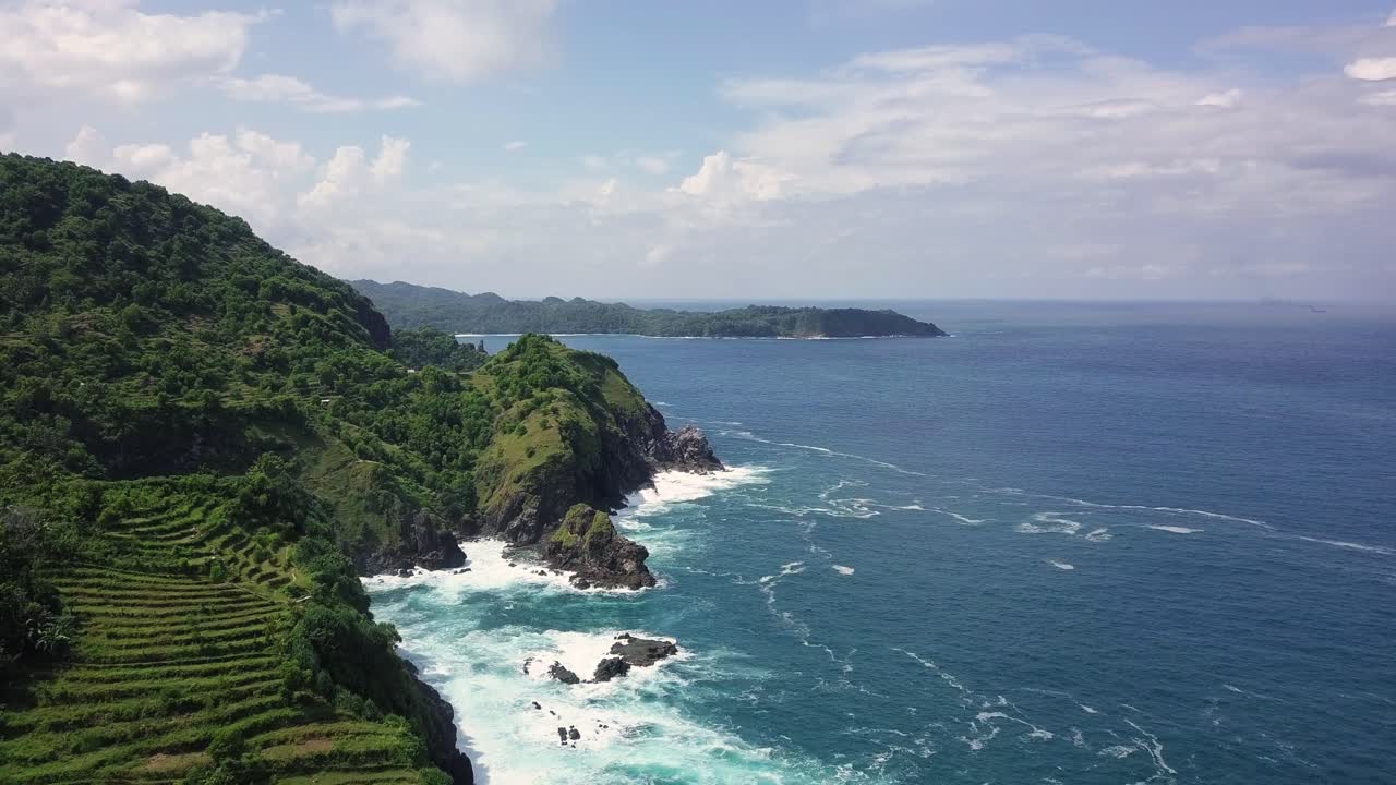 Reveal drone shot over hill overgrown by dense of trees beside blue Ocean in summer - Indonesia,Pengilon Hill