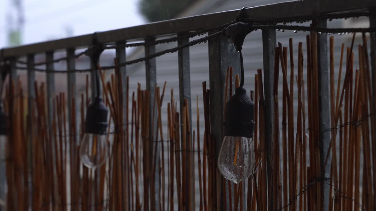 Raindrops trickle down light bulbs and metal railing in this atmospheric rainy-day footage