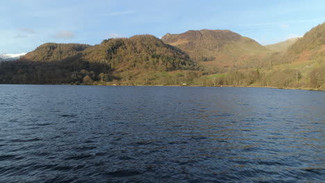 Slow-Low-Aerial-Drone-Shot-Flying-Over-Ullswater-Lake-on-Sunny-and-Cloudy-Morning-with-Hills-and-Trees-in-Background-Lake-District-Cumbria-United-Kingdom