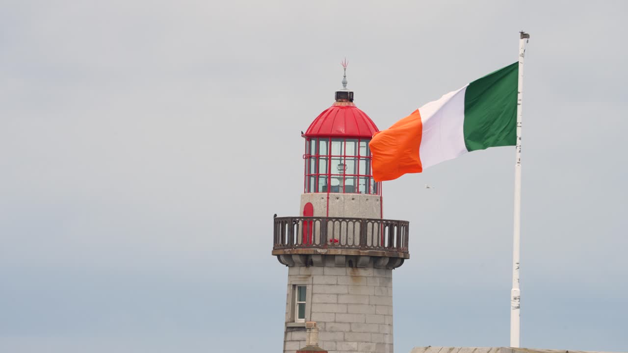 Filmato 4K a 60 fps di un faro nel porto di Dublino, bandiera irlandese che sventola al vento in una giornata nuvolosa