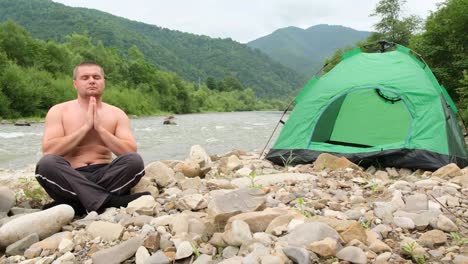 the fat man practices yoga near a mountain river followed by a green tent the fat man practices yoga near a mountain river followed by a green tent outdoor recreation in the mountains