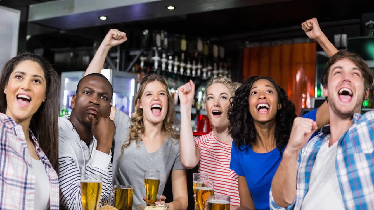 Happy diverse female and male sport fans watching game at bar, cheering and drinking
