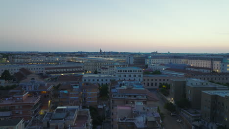 Forwards-fly-above-residential-borough.-Illuminated-buildings-in-city-at-dusk,-colour-twilight-sky.-Rome,-Italy