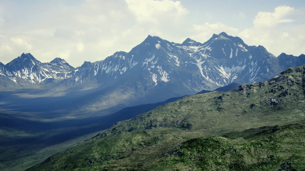 Majestic snow capped mountains rise above green valleys in bright daylight