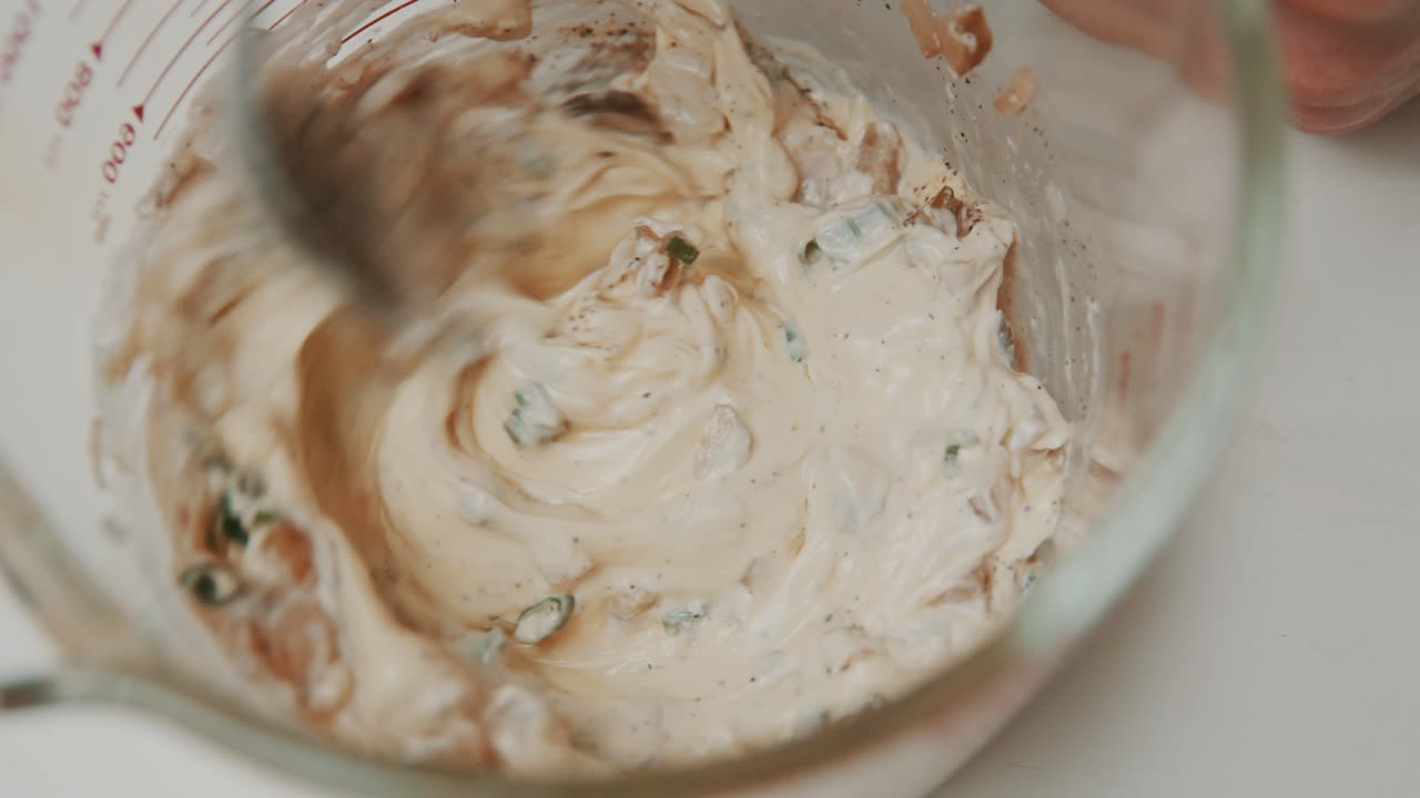 Mixing vegetable sauce ingredients with mayonnaise inside measure glass bowl