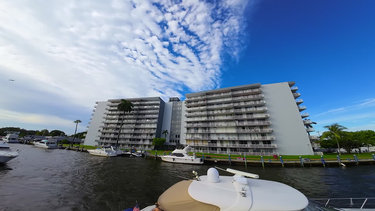 Yachts and boats sail by the narrow river in American city. FPV drone footage on the waterscape under the beautiful azure overcast sky.