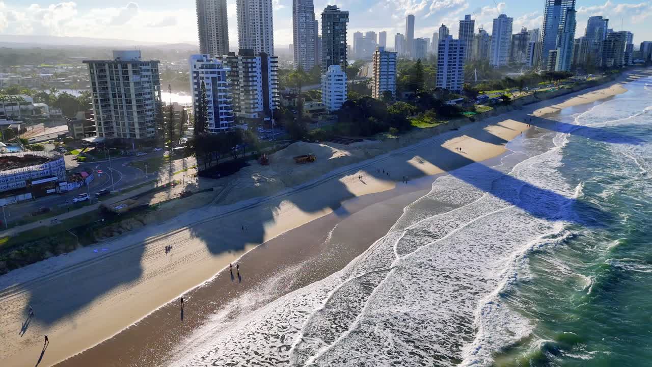 Drone captures Gold Coast's Main Beach with city skyline during sunset, highlighting waves and shadows