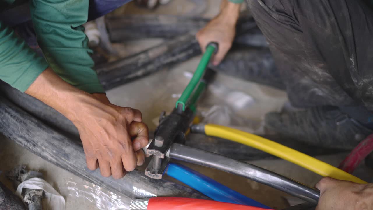 Factory workers crimping heavy duty cable with pliers