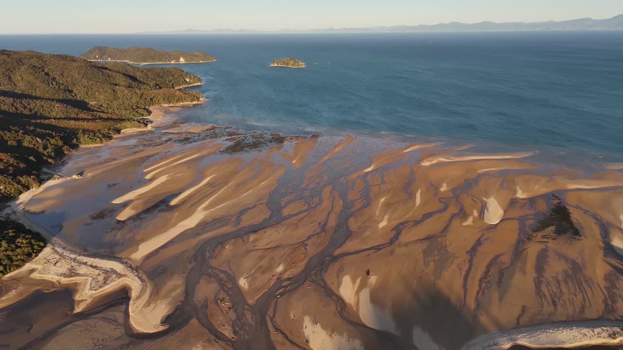 Drone che orbita sopra un estuario di marea con la bassa marea durante l'ora d'oro a Marahau, Nuova Zelanda. Vista panoramica aerea.