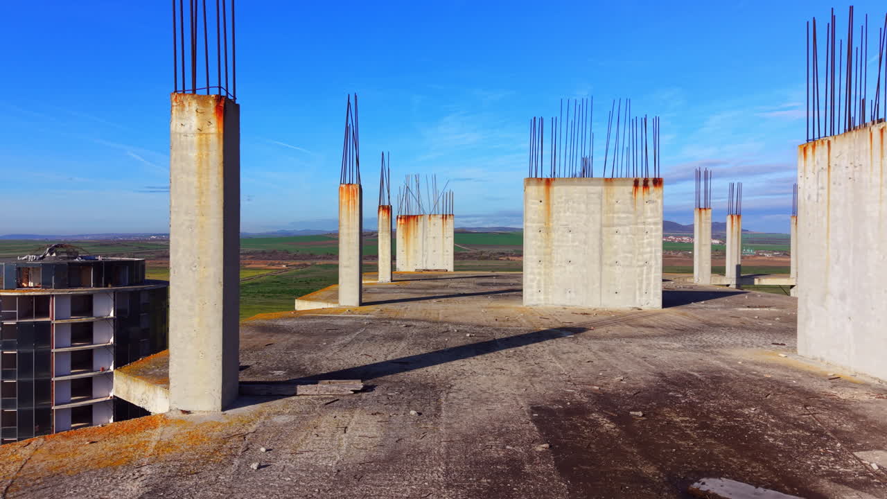 Perspective shot of multiple concrete pillars with rebar on a rooftop. Green fields and hills in the background under a blue sky. Aerial view