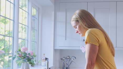 depressed and unhappy mature woman at home standing by kitchen window