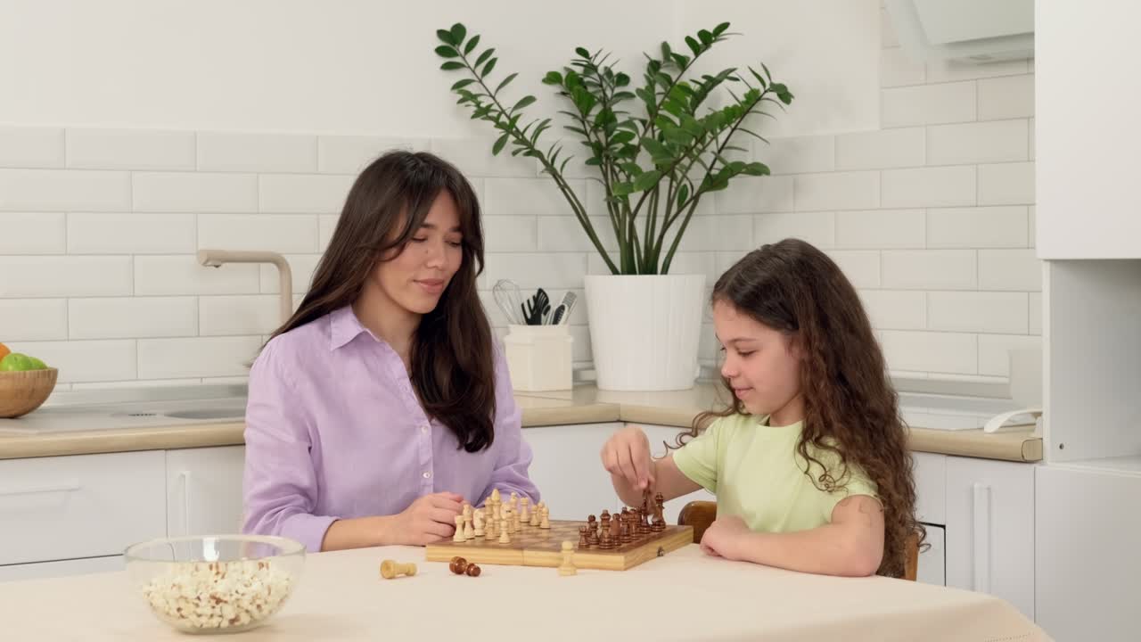madre joven enseña a su hija a jugar al ajedrez sentada en la mesa en casa