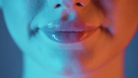primer plano extremo de hermosos labios de mujer llenos con brillo de labios aplicado mientras la mujer simboliza un gesto de alegría con contraste azul naranja en su cara en cámara lenta