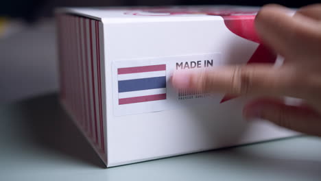 Hands-applying-MADE-IN-THAILAND-flag-label-on-a-shipping-cardboard-box-with-products