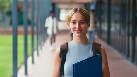 portrait of smiling female high school or secondary student with backpack outside classroom