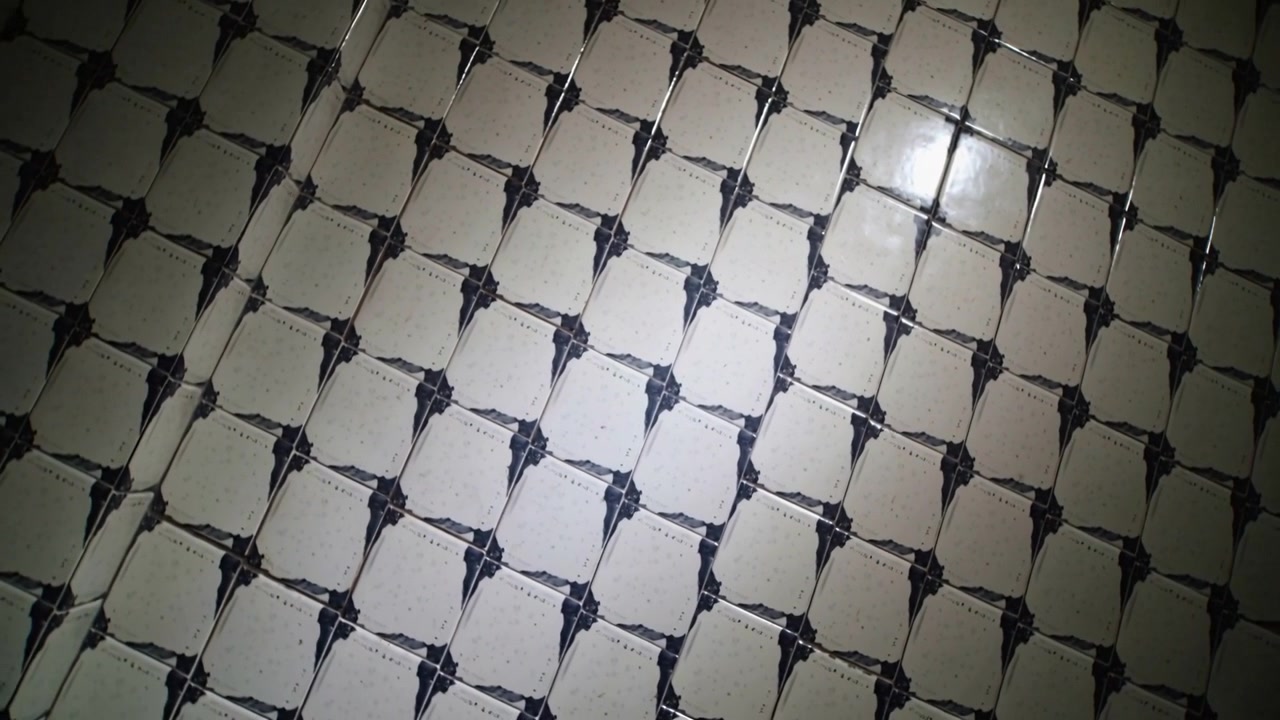 Tilting handheld camera recording glossy ceramic tile grid at room wall, capturing close-up shine