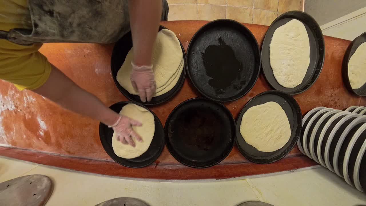 Top down view of worker putting raw pizza dough into deep dish iron cast pans.