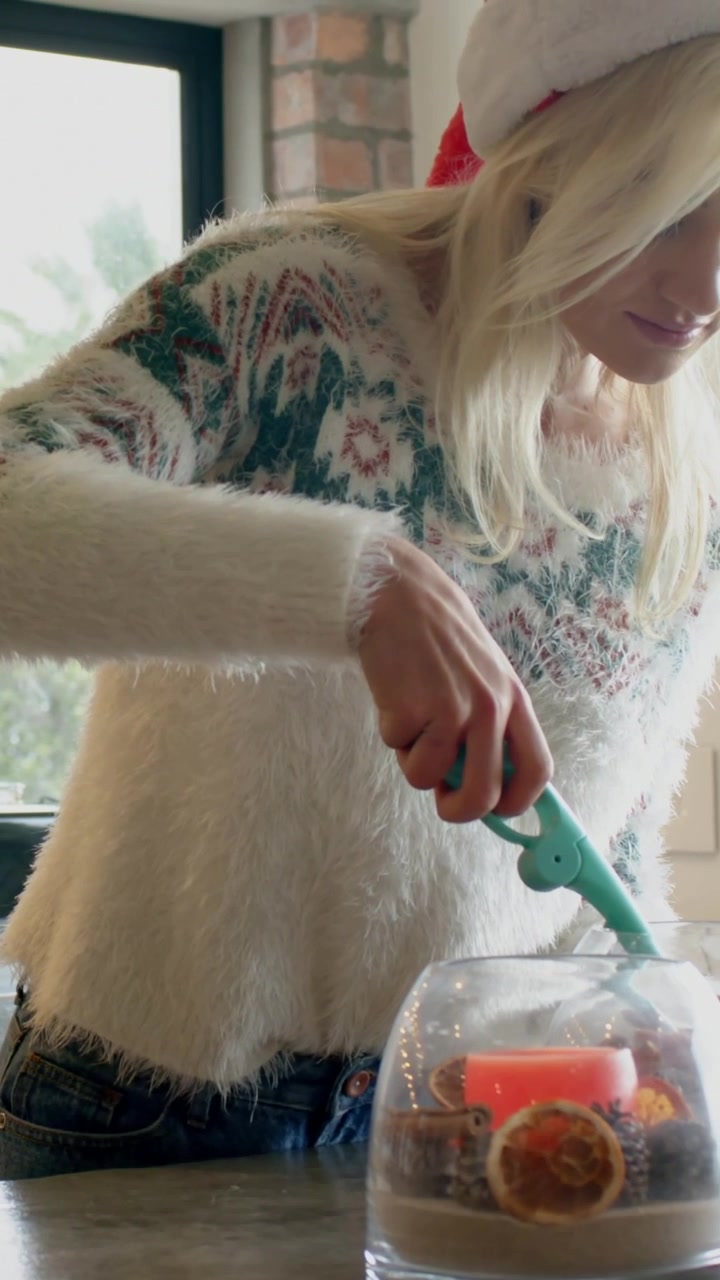 Video verticale: Donna che prepara una candela, indossa un cappello da Babbo Natale e un maglione, prende un accendino in cucina