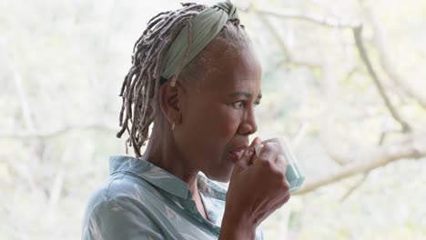 Nachdenkliche-ältere-Afroamerikanische-Frau,-Die-Kaffee-Trinkt-Und-Zu-Hause-Aus-Dem-Fenster-Schaut,-Zeitlupe