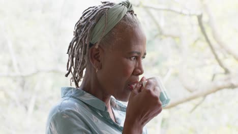 thoughtful senior african american woman drinking coffee and looking out window at home, slow motion