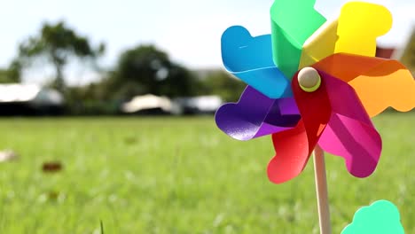 a colorful pinwheel spins energetically against a backdrop of lush grass and distant trees.