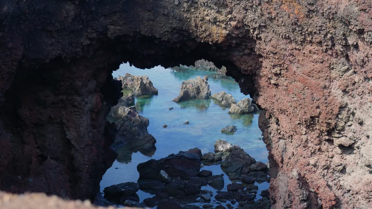 Vista attraverso un arco di roccia vulcanica su un oceano azzurro e cristallino