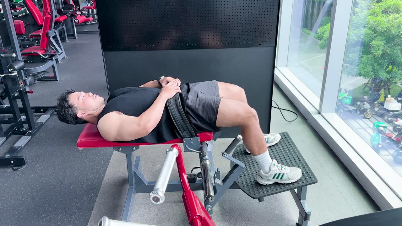 Athletic man executes hip thrusts on bench in bright gym with large windows, natural lighting