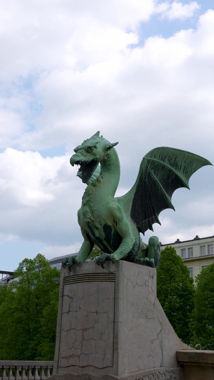 Vista verticale della famosa statua del drago sul Ponte dei Draghi a Lubiana, con ali drammatiche, cielo nuvoloso e dettagli iconici del punto di riferimento della città slovena