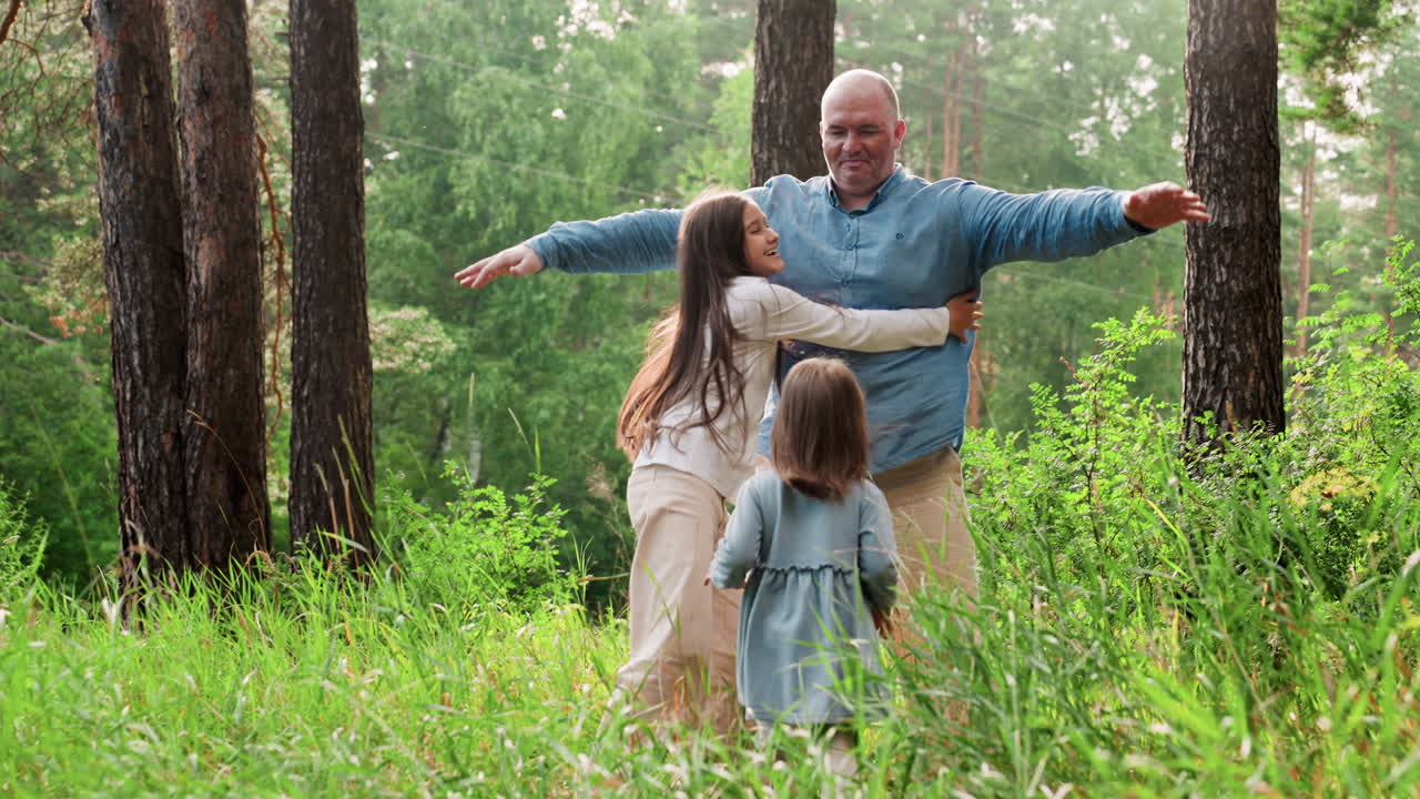 Breadwinner spreading hands wide with joy as daughters run toward him in excitement during cheerful family hangout in green forest, capturing warm emotional reunion moment